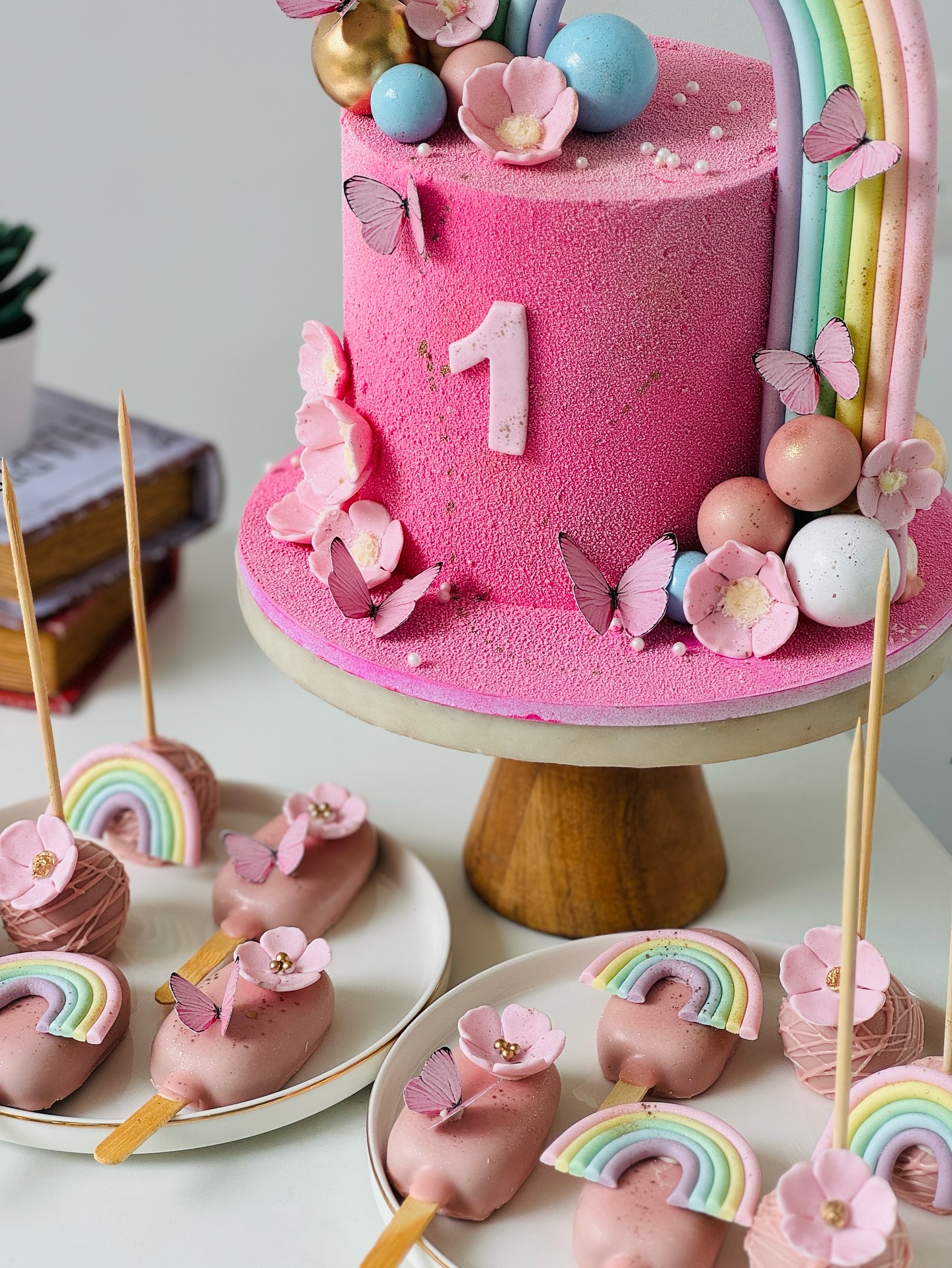 Pink rainbow first birthday cake with butterflies and dessert styling